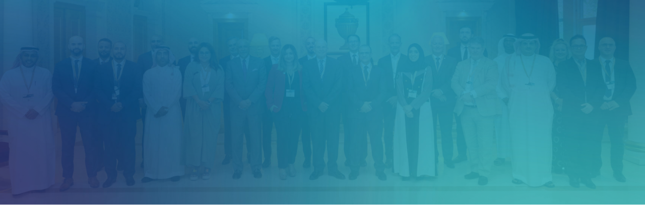  This image portrays a large group of professionals posing together for a group photograph. The individuals are dressed in a mix of business attire, including suits and traditional Middle Eastern garments. The setting appears formal, likely a conference or a business event, with ornate background elements that suggest an upscale venue. The diversity of the group in terms of gender and ethnicity reflects a global or multicultural meeting or conference.